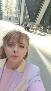 Image is of Leslie in pastel rainbow tailored suit outside an office in London UK