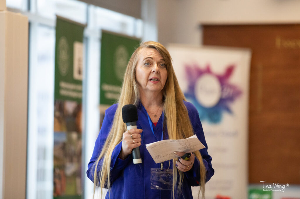 picture of leslie speaking at the Health and Wellbeing conference in Essex.  She is wearing a blue shirt and has a microphone in her hand. and is speaking about ADHD in the workplace